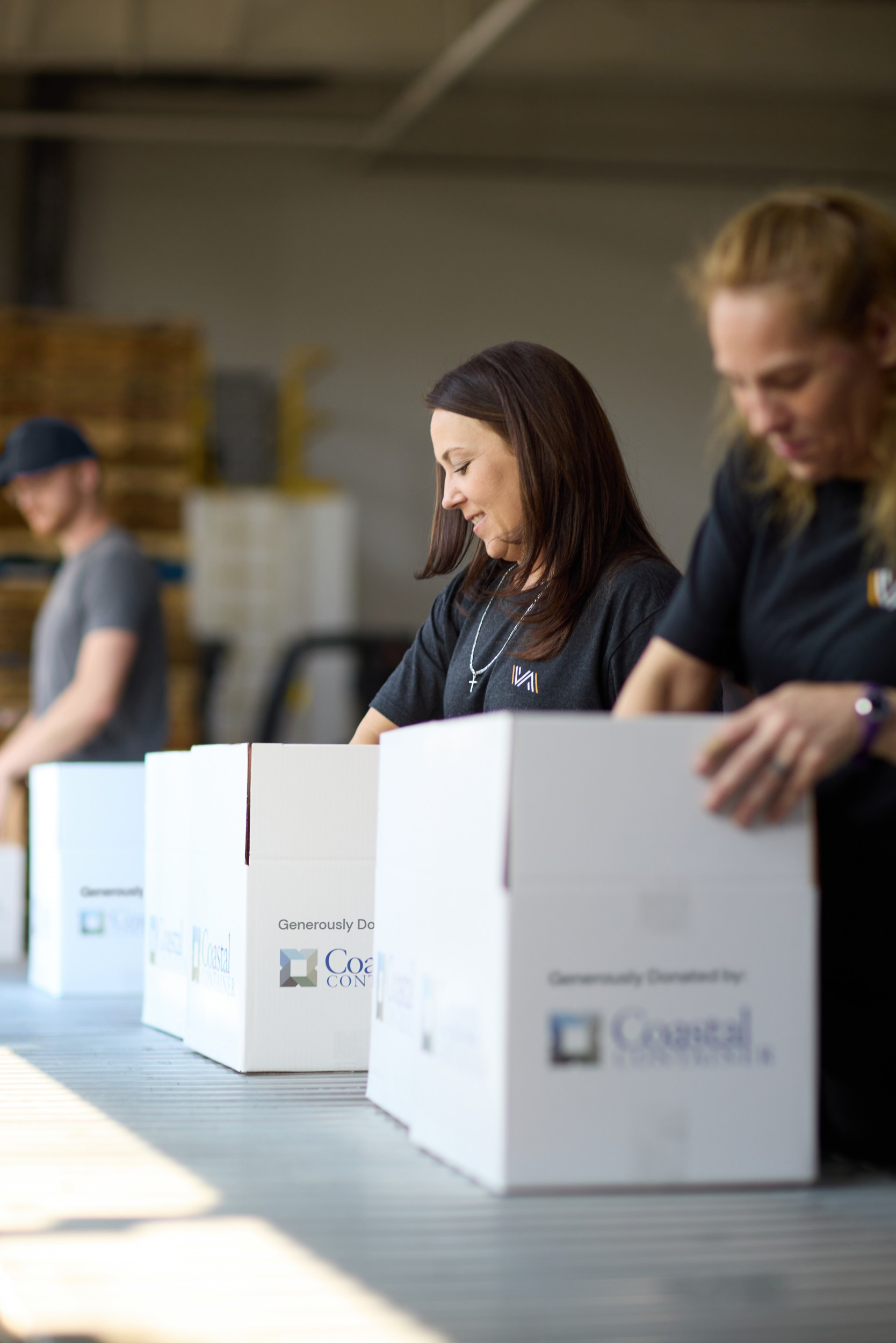 A smiling woman wearing a gray shirt with a VAFS logo and a cross necklace packing white boxes. 